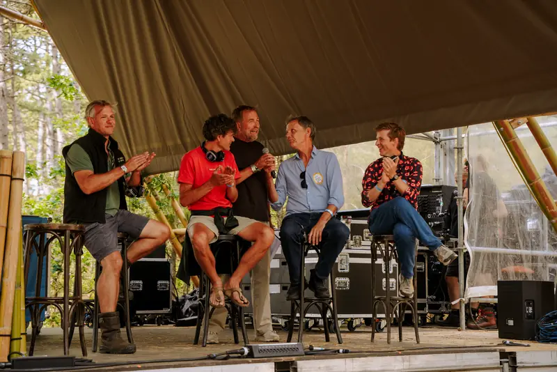 Vijf sprekers op het podium onder een dak van bamboe