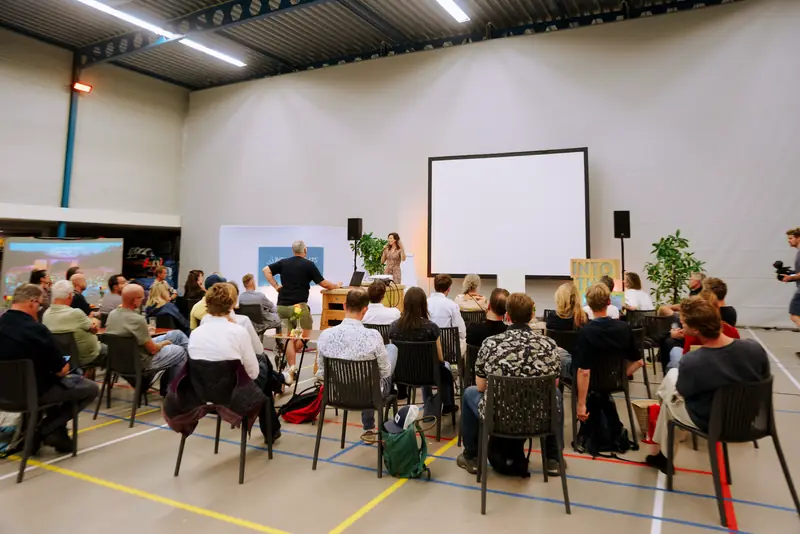 Een volle zaal luistert naar een presentatie